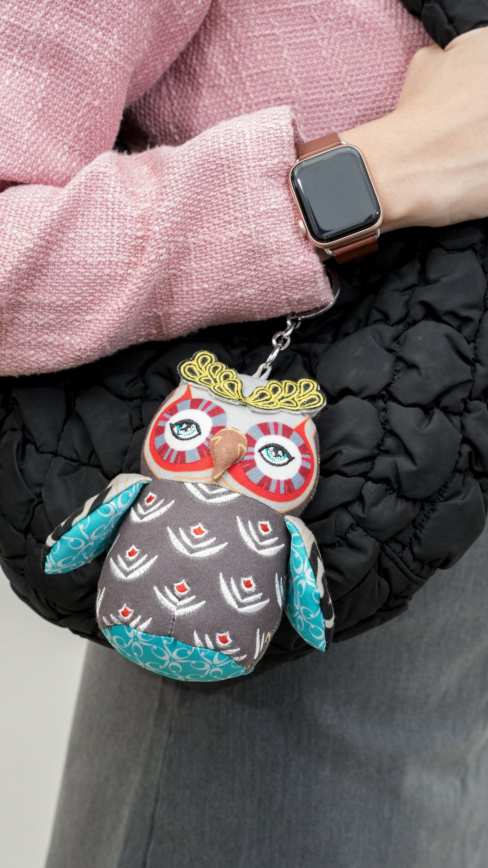 Person wearing a black coat with a colorful owl-shaped keychain attached to it.