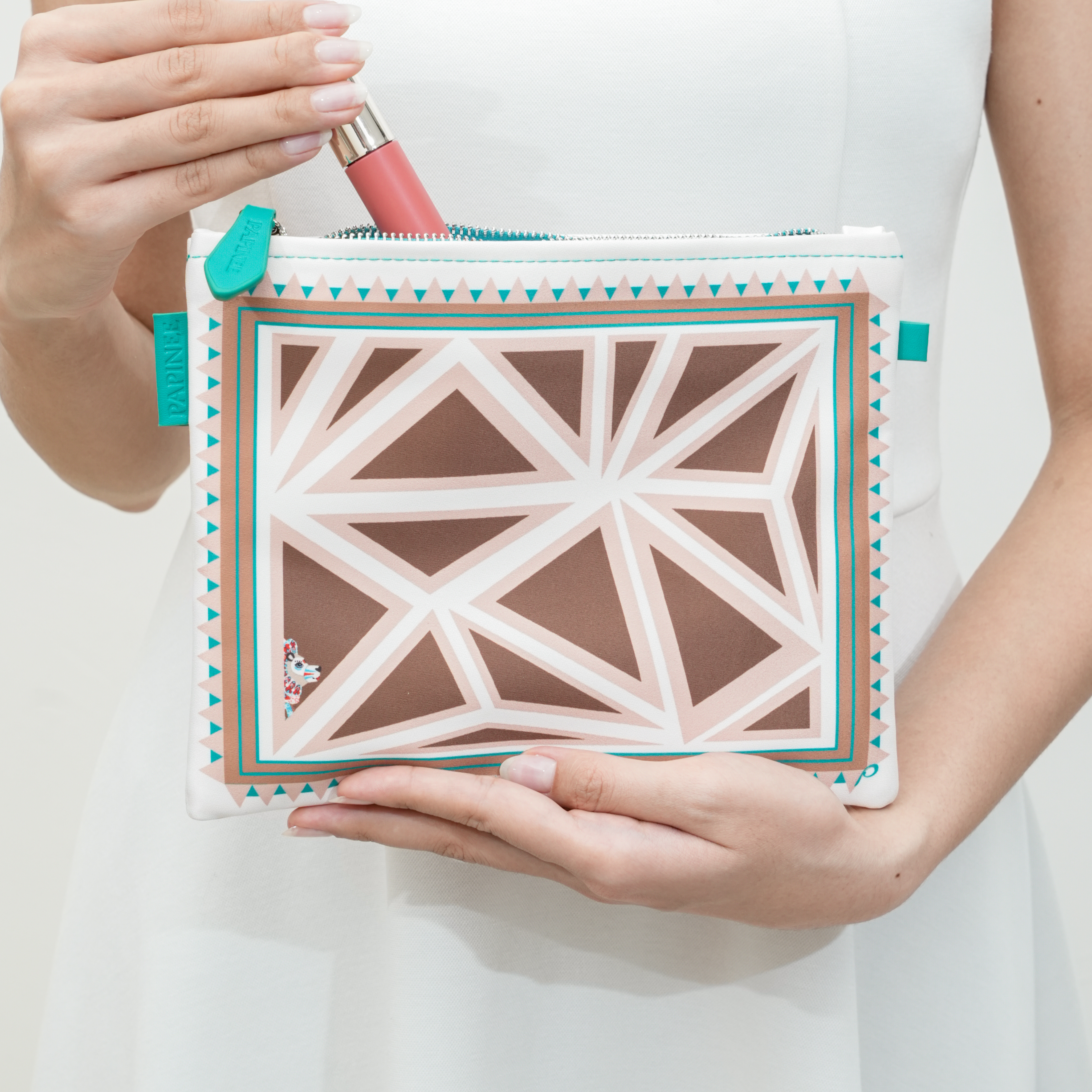 Person holding a geometric-patterned pouch with a lip tint inside on a white background